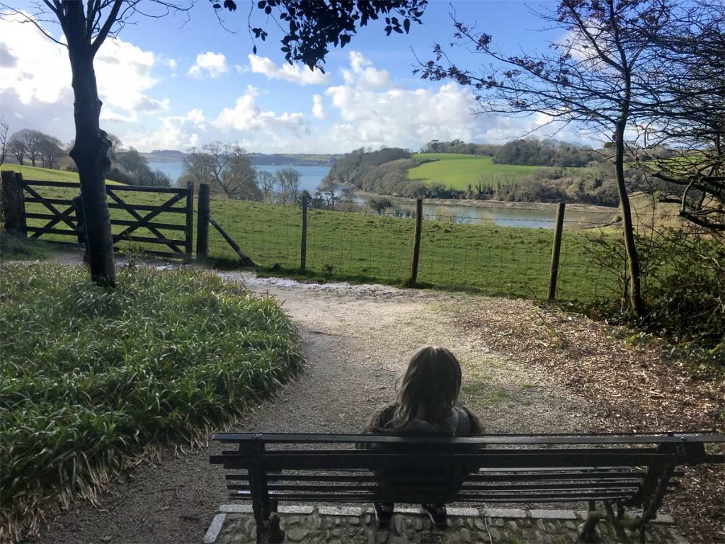 Girl sitting on a bench and enjoying the tranquillity and view over the River Fal at Trelissick Gardens
