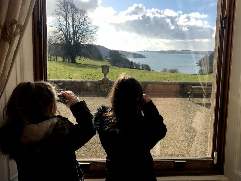 Two girls admire the view over the River Fal from a window Trelissick house